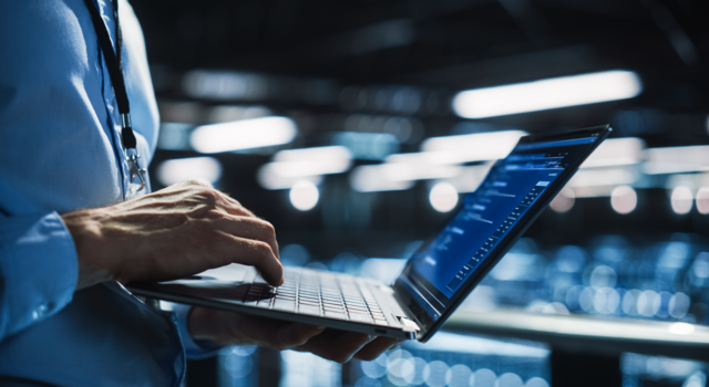 Technicien informatique consultant des données sur son ordinateur portable dans une salle de serveurs