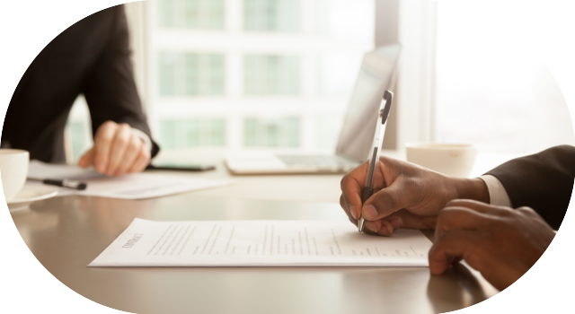 Main d’un professionnel signant un contrat sur un bureau, en présence d’un autre collaborateur