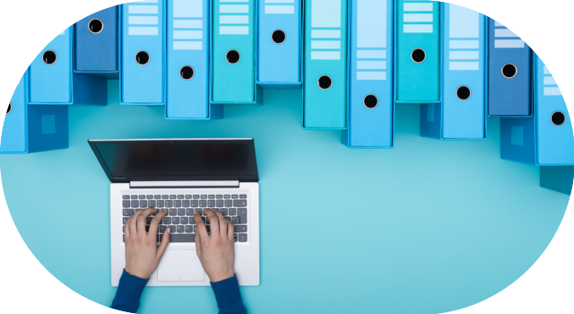 Mains tapant sur un ordinateur entouré de classeurs bleus symbolisant l’archivage digital